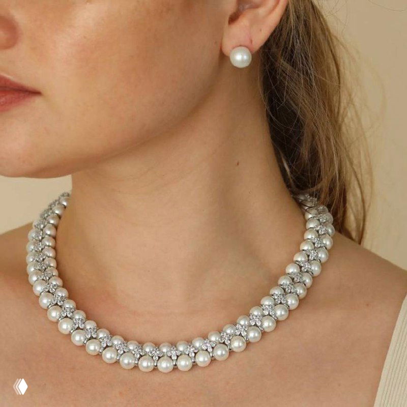 Классическое жемчужное колье и жемчужная серьга на шее модели в светлом образе — универсальное украшение для делового и праздничного стиля.