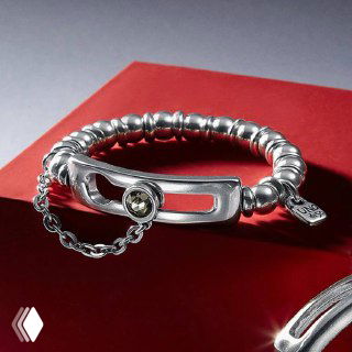 Массивный серебристый браслет с декоративной застёжкой и цепочкой, представленный на тёмно-красном фоне — украшение в минималистичном стиле.