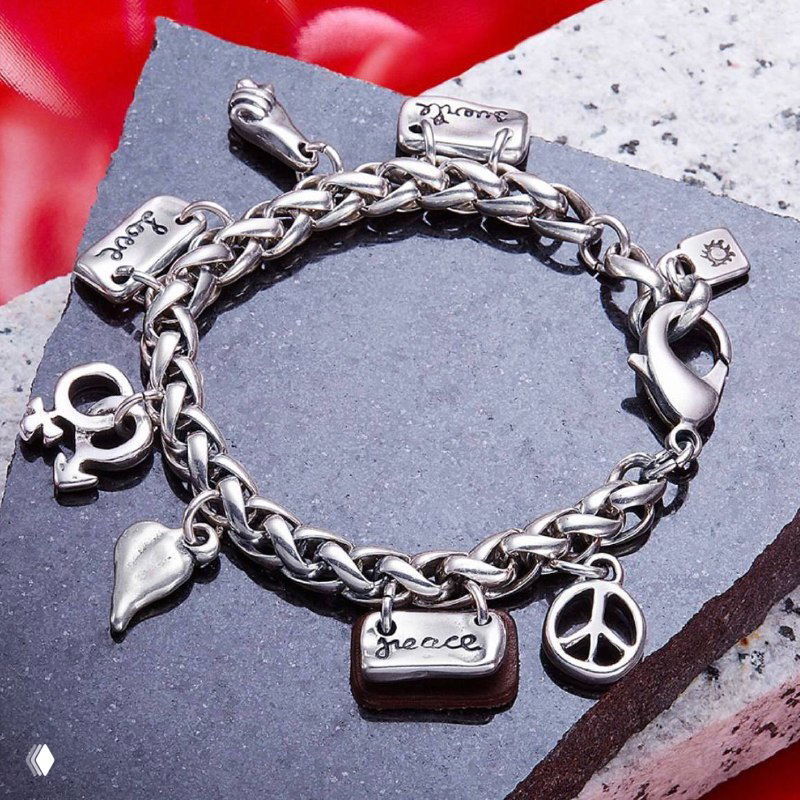 Браслет-цепочка UNOde50 с множеством подвесок — сумочка, сердце, знак мира и другие шармы, детальная съемка на фактурной поверхности для каталога бренда