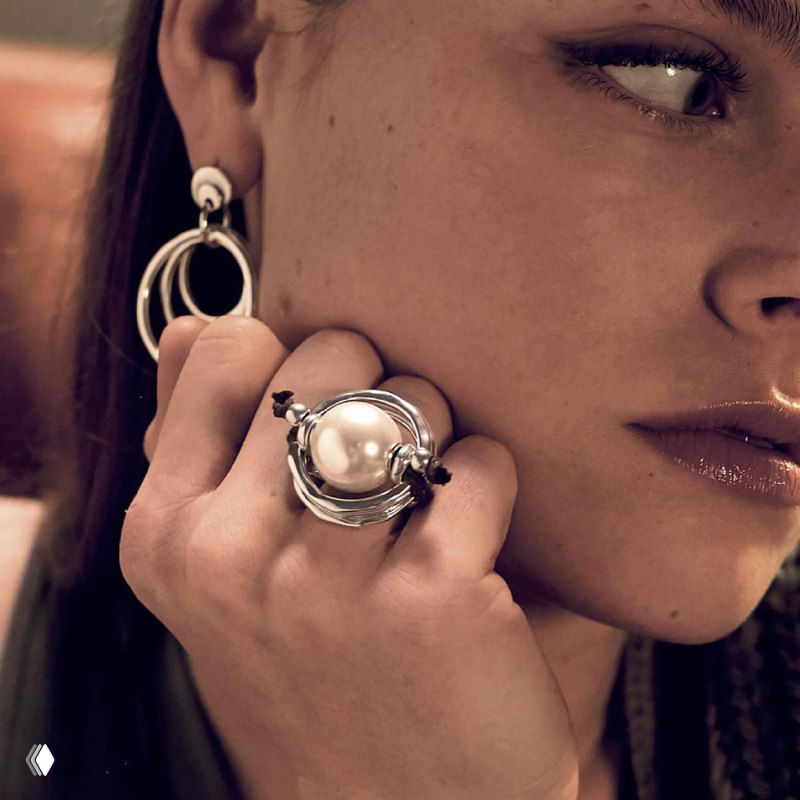 Девушка демонстрирует крупное кольцо с жемчужиной и массивные серьги UNOde50; кадр подчёркивает фактуру металла и дизайн украшения, рекламная фотография