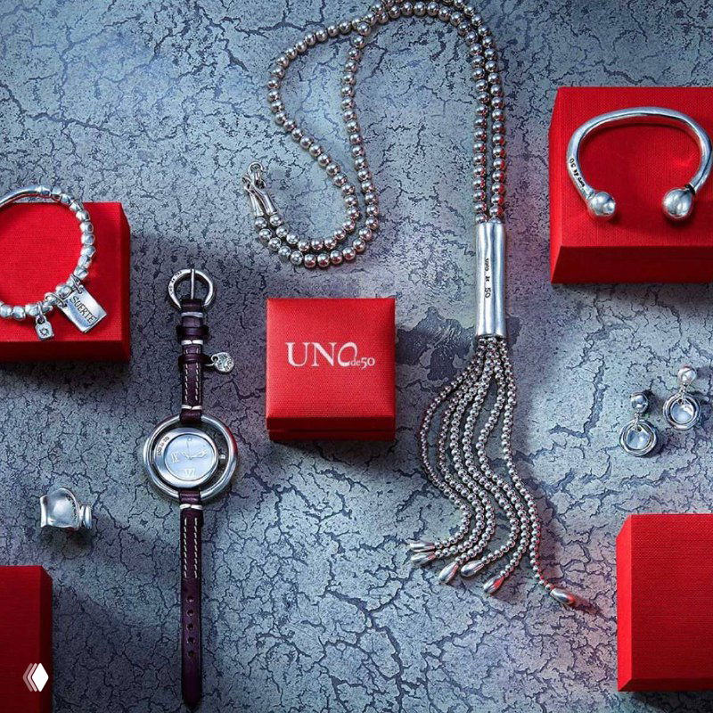 Коллаж из часов, подвесок и фирменных красных коробок UNOde50 на текстурированной поверхности — рекламная композиция коллекции аксессуаров и подарочной упаковки