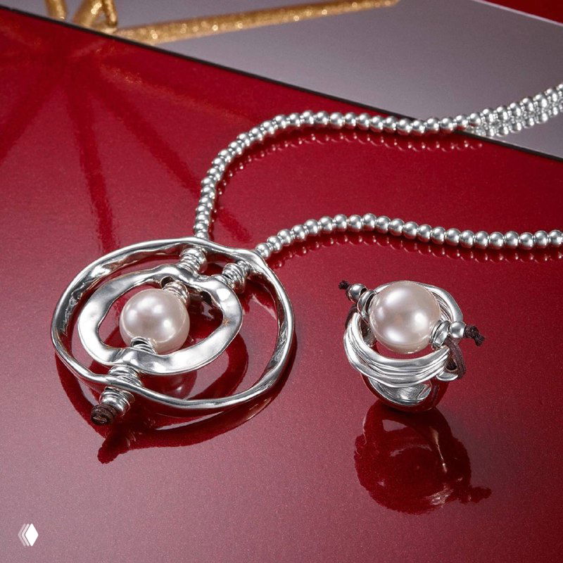 Рекламная композиция: серебряный комплект UNOde50 с жемчужной подвеской и кольцом на глянцевом красном фоне, студийная съемка для презентации коллекции