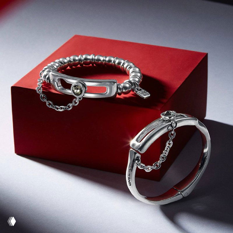 Два серебряных браслета UNOde50, расположенные на красном подиуме; детальная съемка фурнитуры и цепочек, стильная презентация товарного образа для каталога