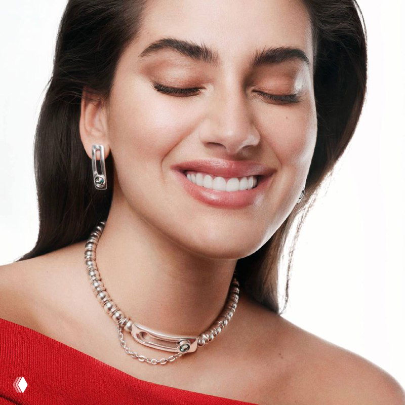 Улыбающаяся модель в светлой одежде с цепочным ожерельем и серьгами UNOde50; рекламный портрет с акцентом на женскую аудиторию и носибельность аксессуаров