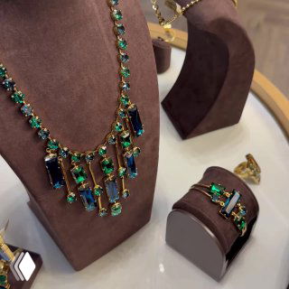 Коллекция украшений Claudio Canzian: крупная колье-цепь с зелёными и синими вставками на бархатном манекене в витрине магазина.