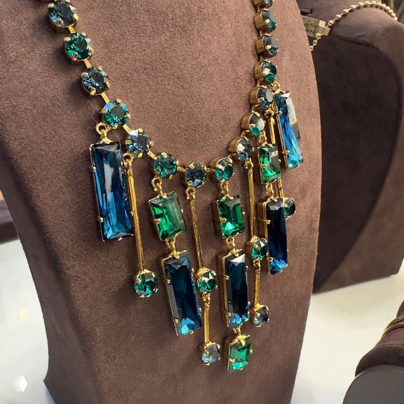 Близкий план декоративного колье с крупными синевато-зелёными стразами и золотыми вставками — образец украшений коллекции Claudio Canzian 2024.