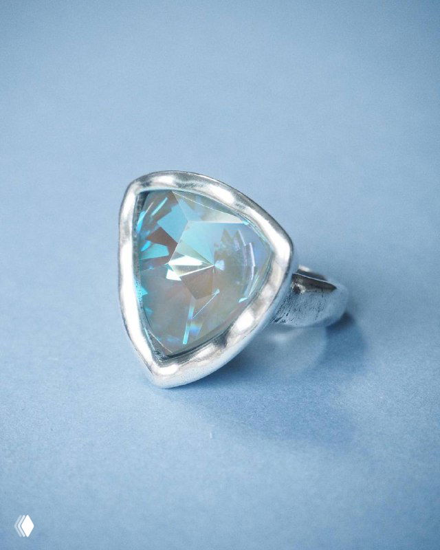 Крупный план серебряного кольца с треугольным голубым кристаллом Swarovski на светло-голубом фоне, студийная подсветка