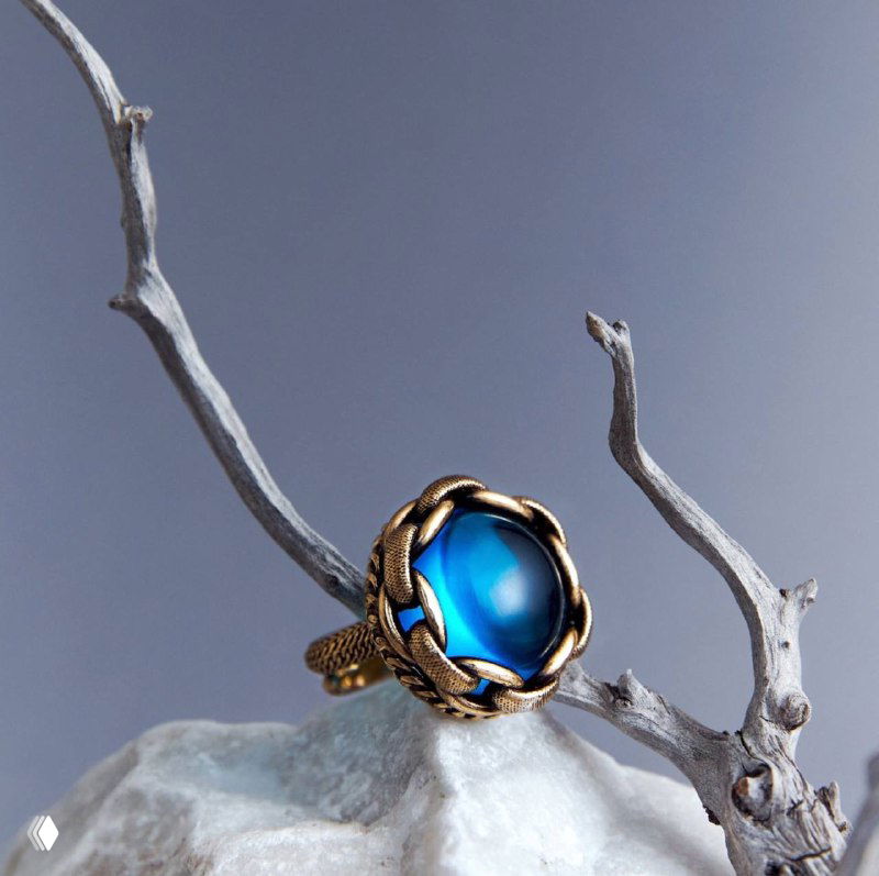 Кольцо CATENE крупным планом на ветке: полупрозрачное сине-зеленое стекло, обрамленное грубыми цепными звеньями.