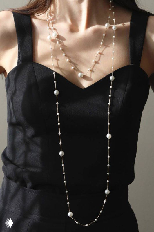 Женский торс в чёрном платье с длинным жемчужным колье-нить Uvelina длиной 190 см, снято спереди, демонстрация многослойного варианта носки и длины украшения.