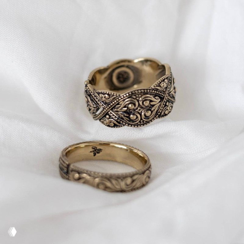 Два золотистых кольца с филигранной резьбой на белой ткани, крупный план для презентации текстуры и винтажной отделки изделий бренда Fiore di Firenze.