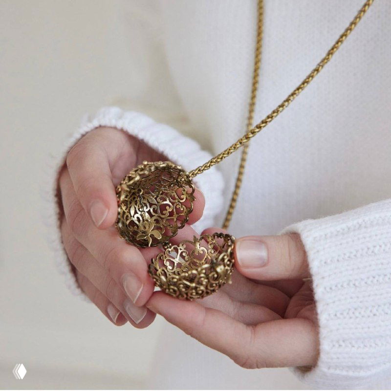 Два ажурных кулона-шара в руках модели на золотой цепочке, демонстрация размера и редко встречающегося дизайна Fiore di Firenze.
