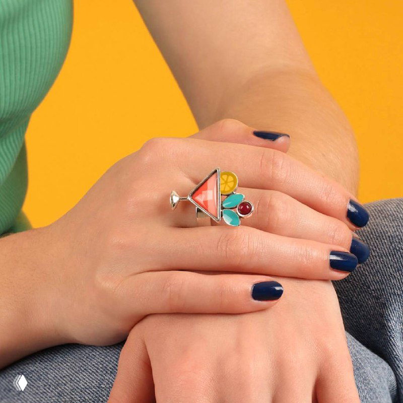 Рука модели с несколькими кольцами TARATATA, одно кольцо геометрической формы с цветными вставками на жёлтом фоне — образ в стиле casual.