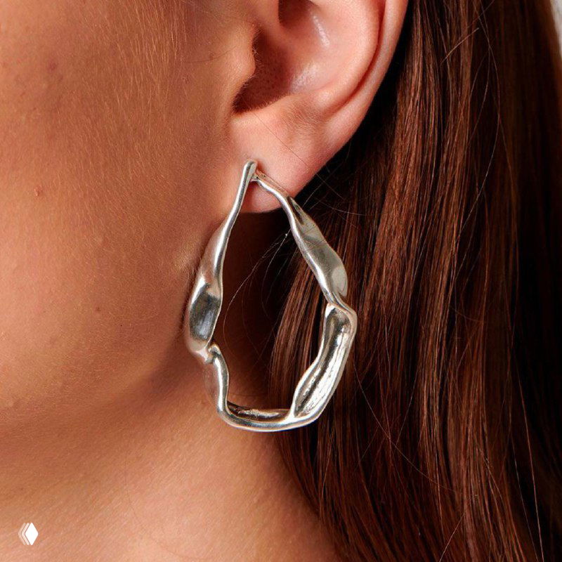 Серьги UNOde50 на ухе модели: художественный кадр, показывающий форму и фактуру мятого металла в повседневном образе.