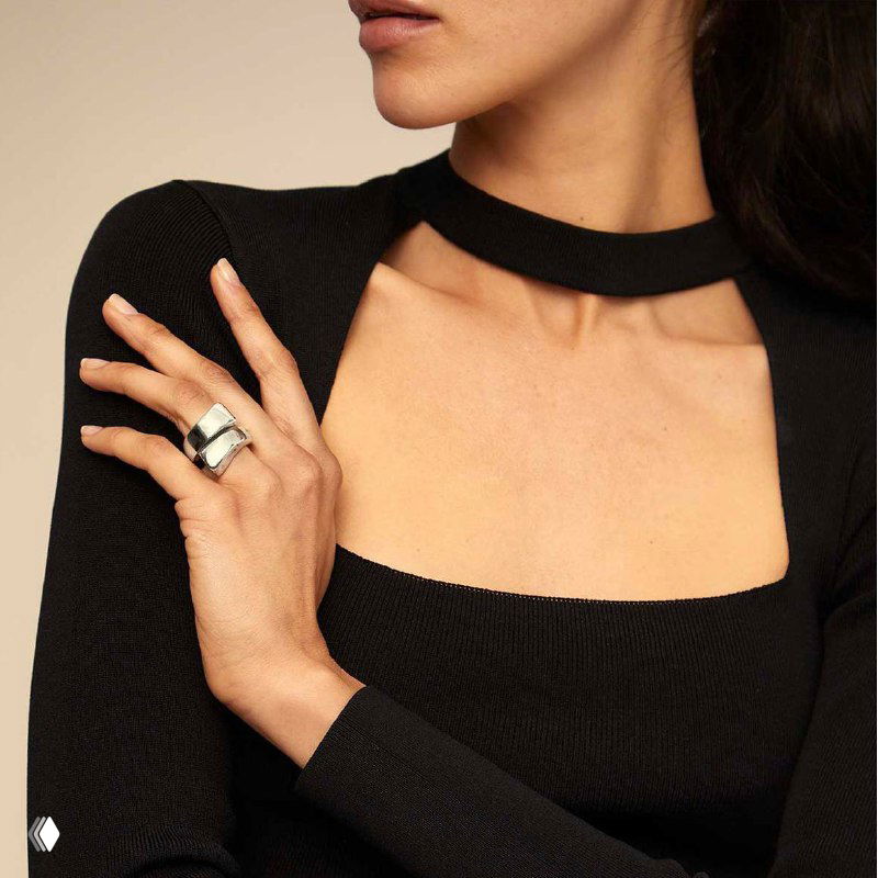 Женская рука с кольцом UNOde50 на фоне чёрного наряда: кадр подчёркивает дизайн кольца и сочетание с одеждой.