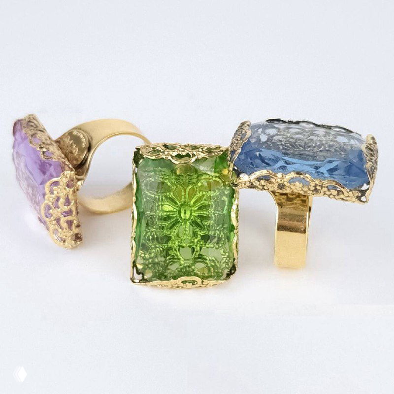 Три декоративных кольца с крупными окрашенными камнями — сиреневым, зелёным и голубым — на светлом фоне, акцент на форме и оправе.