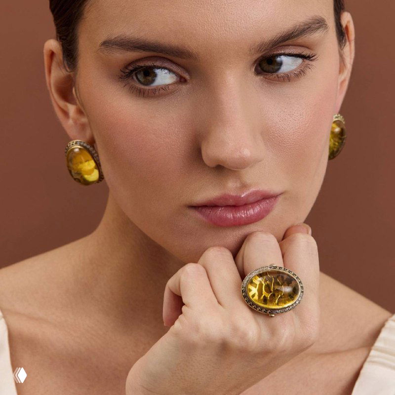 Портрет женщины, демонстрирующей большое коктейльное кольцо с янтарным или жёлтым камнем и подходящие серьги, образ в нюдовых тонах.