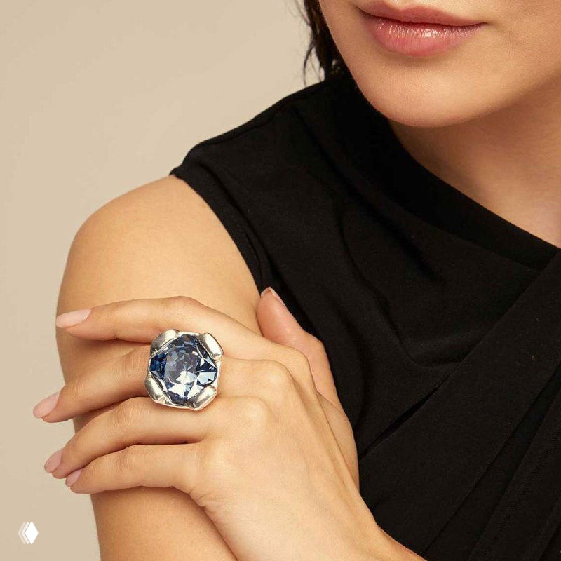Рука женщины в чёрном платье, на пальце крупное кольцо с большим голубым камнем — украшение подчёркивает вечерний образ и элегантность.