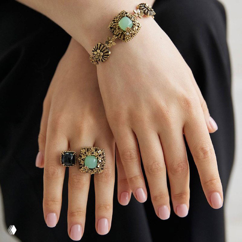 Несколько рук с разными крупными кольцами и браслетом в винтажном стиле — сочетание массивных форм и пастельных камней на тёплом фоне.