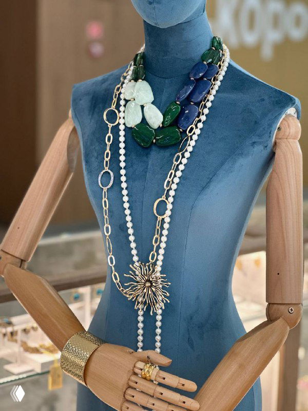 Манекен в витрине, на котором показаны многослойные ожерелья и браслеты: зеленые камни, жемчуг и крупная подвеска в составе коллекции бижутерии.