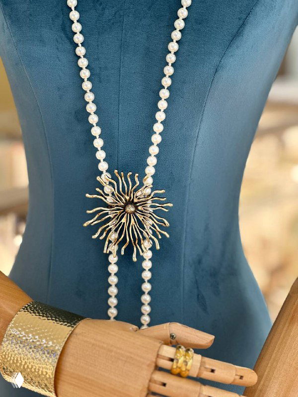 Манекен, украшенный длинной жемчужной нитью и центральной солнечной подвеской, дополненной золотистыми акцентами — витрина бижутерии Rosone.