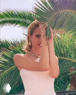 Модель в белом платье демонстрирует украшения DYRBERG/KERN — серьги, браслет и колье на фоне пальм; рекламная съёмка для магазина Rosone.