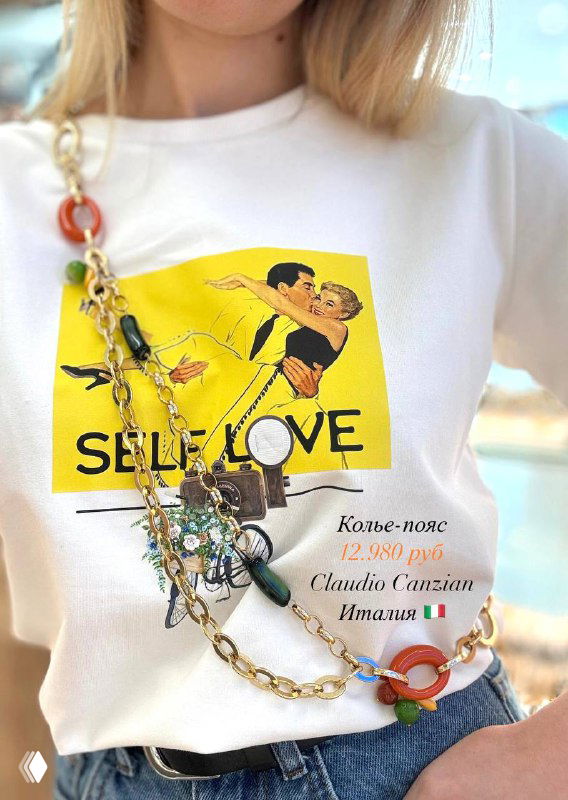 Удлинённое колье-цепь с крупными яркими вставками и декоративными деталями на фоне белой футболки с принтом.