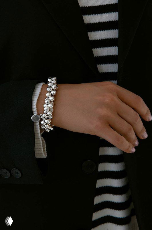 Крупный план на запястье модели в пальто: элегантный браслет Ciclon из полированных шариков дополнит повседневный образ и пальто.
