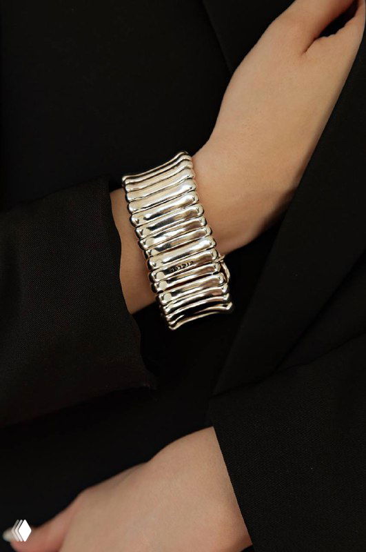 Запястье модели, одетой в черный пиджак, украшено широким текстурным браслетом Ciclon серебристого оттенка — образной съемка аксессуара.