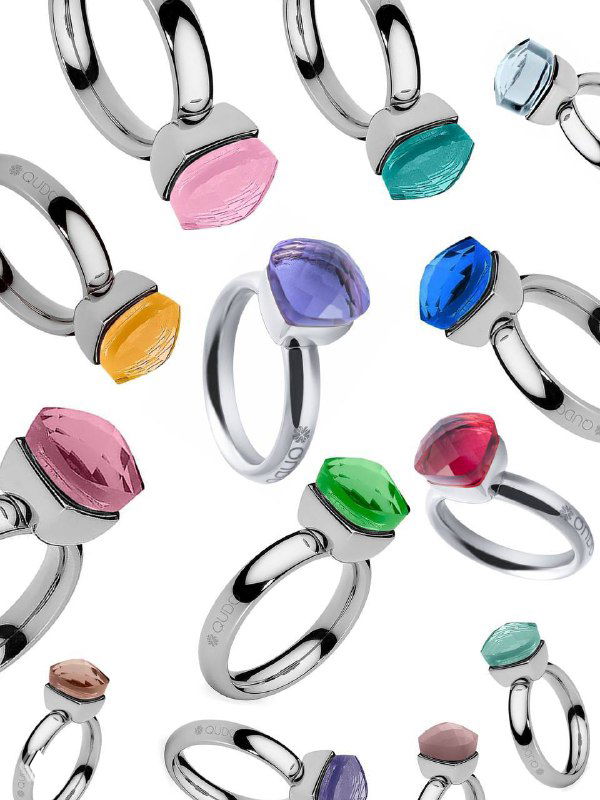 Ряд серебристых колец Qudo с яркими гранёными кристаллами Swarovski разных оттенков на белом фоне — демонстрация палитры бренда.