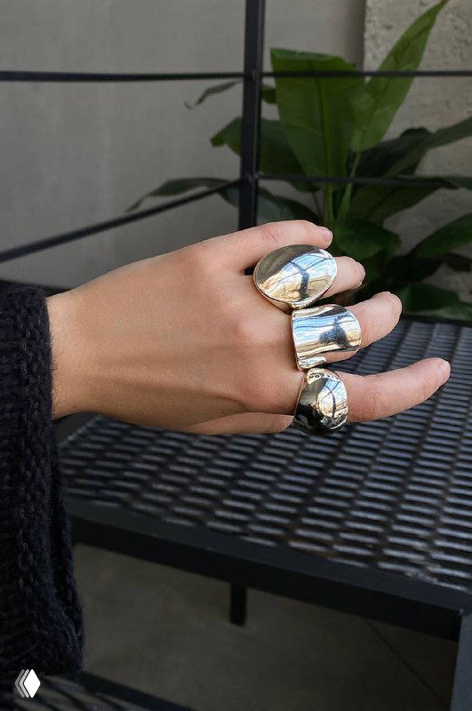 Рука с несколькими крупными кольцами Ciclon, снятая на уличной поверхности — демонстрация фактуры и масштаба украшений в реальном образе.