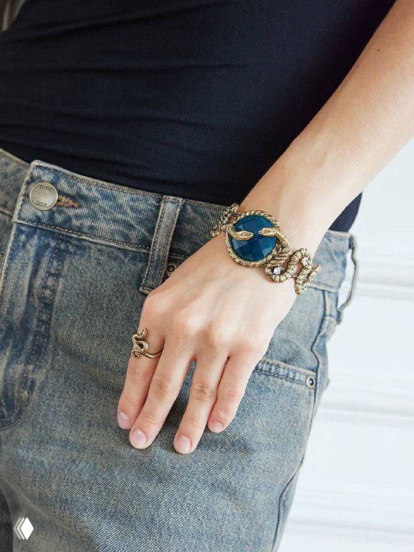 Крупный план запястья в джинсах: браслет Serpenti с центральным синим кристаллом и змеиным декором по бокам.