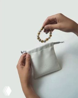Женские руки на светлом фоне держат браслет из бусин над элегантным мягким мешочком для хранения украшений, логотип Vidda виден.