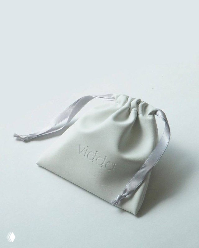 Крупный план мягкого белого мешочка с затягивающими шёлковыми лентами на светлом фоне — упаковка для хранения украшений в магазине.