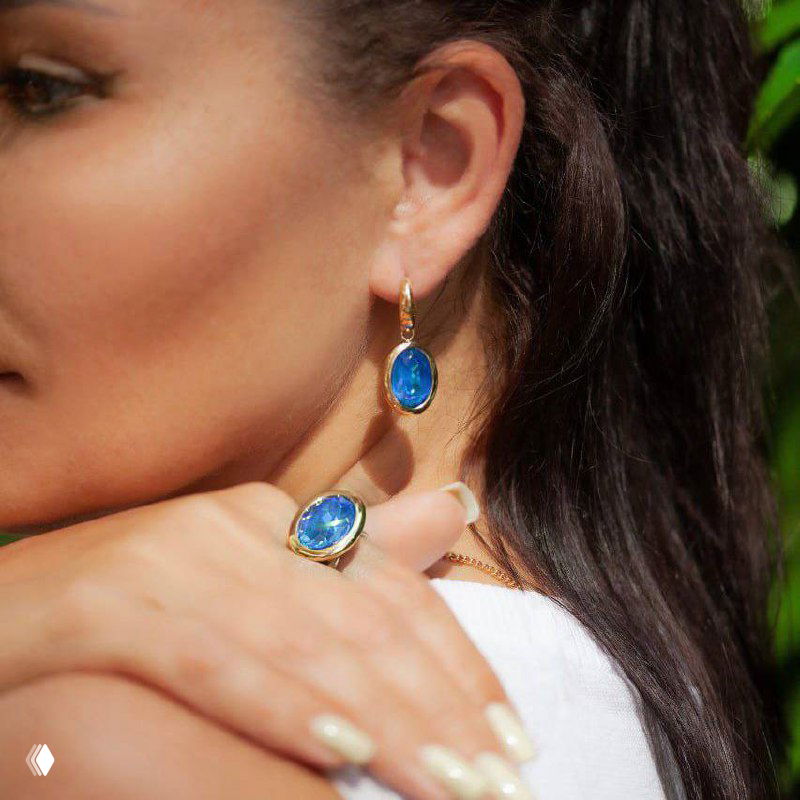 Модель в профиль в серьгах и кольце QUDO с синими кристаллами, показ посадки украшений на шее и кисти руки