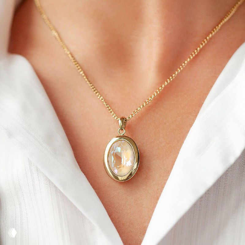 Колье QUDO с овальной подвеской на тонкой золотой цепочке на шее — позолоченная оправа и прозрачный кристалл на фоне белой блузы