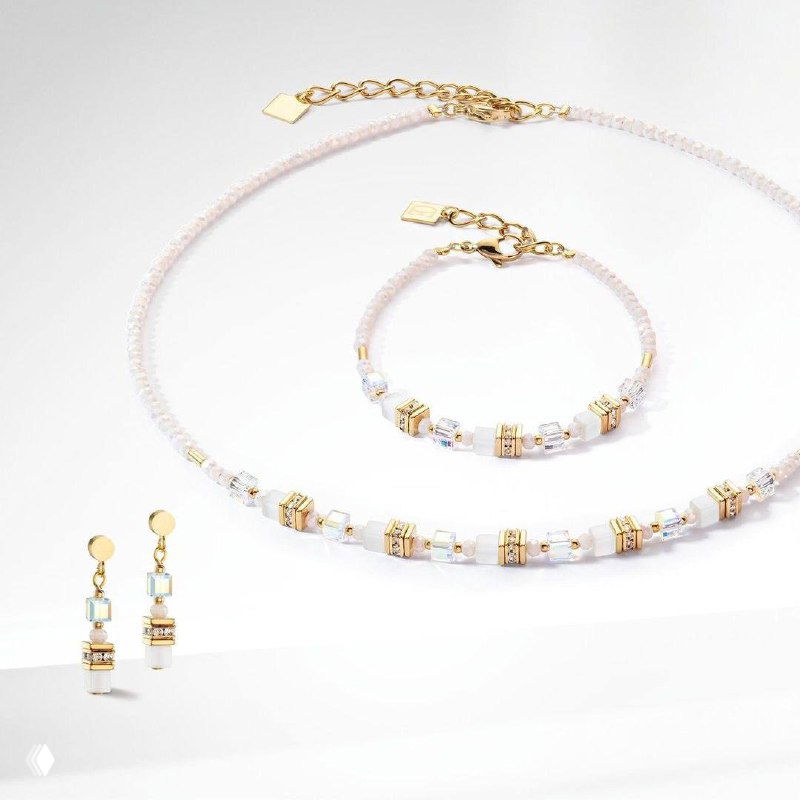 Крупный план кремового ожерелья и браслета Coeur de Lion с золотыми вставками и пара серьг на светлом фоне — детализированная студийная композиция.