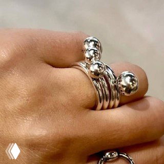 Крупный план сложенного набора серебристых колец с шариками на пальце модели; текстура металла и отражения на поверхности.