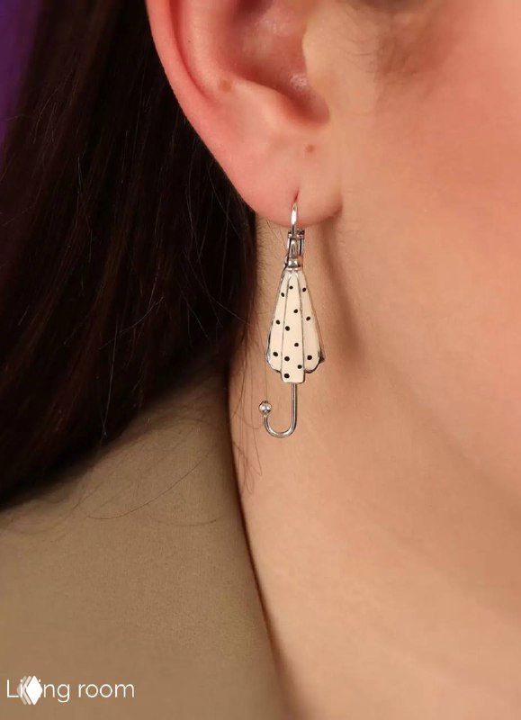 Серьга в виде зонтика из коллекции Living room на ухе модели — серебристая эмаль с черными точками, показывает как сидит украшение.