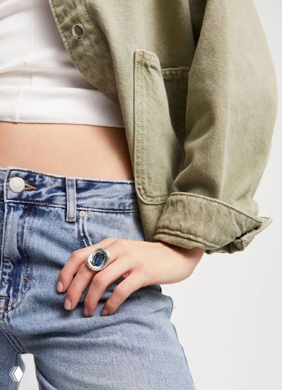 Фрагмент образа: модель в джинсах и крупном кольце UNOde50 с синим кристаллом, демонстрация повседневного стиля с бижутерией бренда.