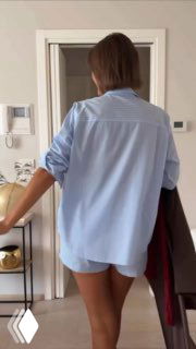 Частный кадр: женщина в голубой рубашке и коротких шортах стоит спиной в светлом интерьере, создавая уютный образ.