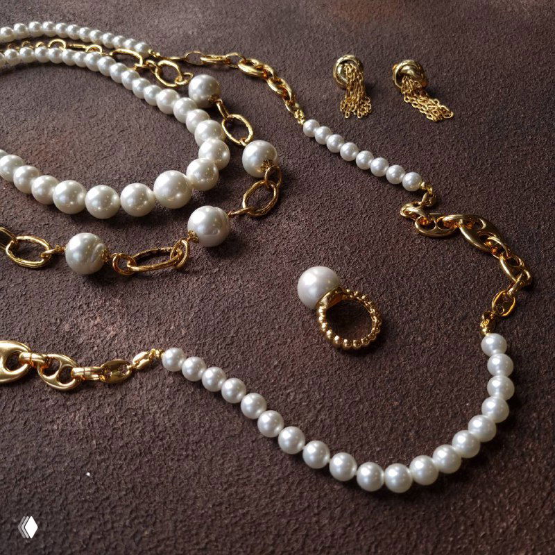 Несколько украшений: бусы, колье и серьги с жемчугом и золотыми звеньями на темном фоне — ассортимент Madreperla.