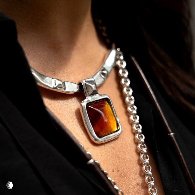 Крупный план кулона с тёмно-янтарной вставкой муранского стекла в серебряной оправе на цепочке, подчёркнут тёплый осенний оттенок и фактура стекла