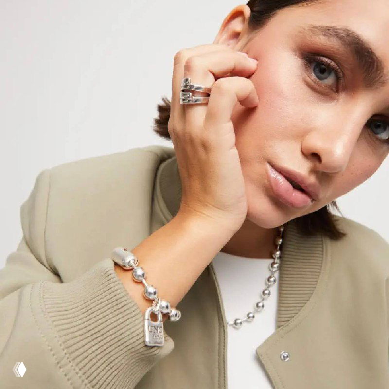 Женщина в светлой куртке демонстрирует серебристый браслет Snowflake с подвеской-замком и заметной декоративной застёжкой — повседневный аксессуар.