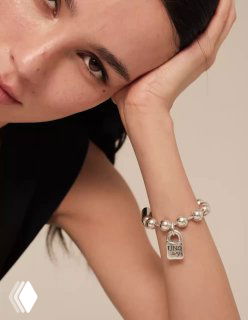 Крупный план запястья модели в лаконичном образе: браслет Snowflake с характерной подвеской-замком и гладкими шариковыми звеньями.