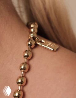 Макросъёмка золотого браслета Snowflake: видна застёжка и подвеска-таблетка с фирменным тиснением, деталь украшения вблизи.