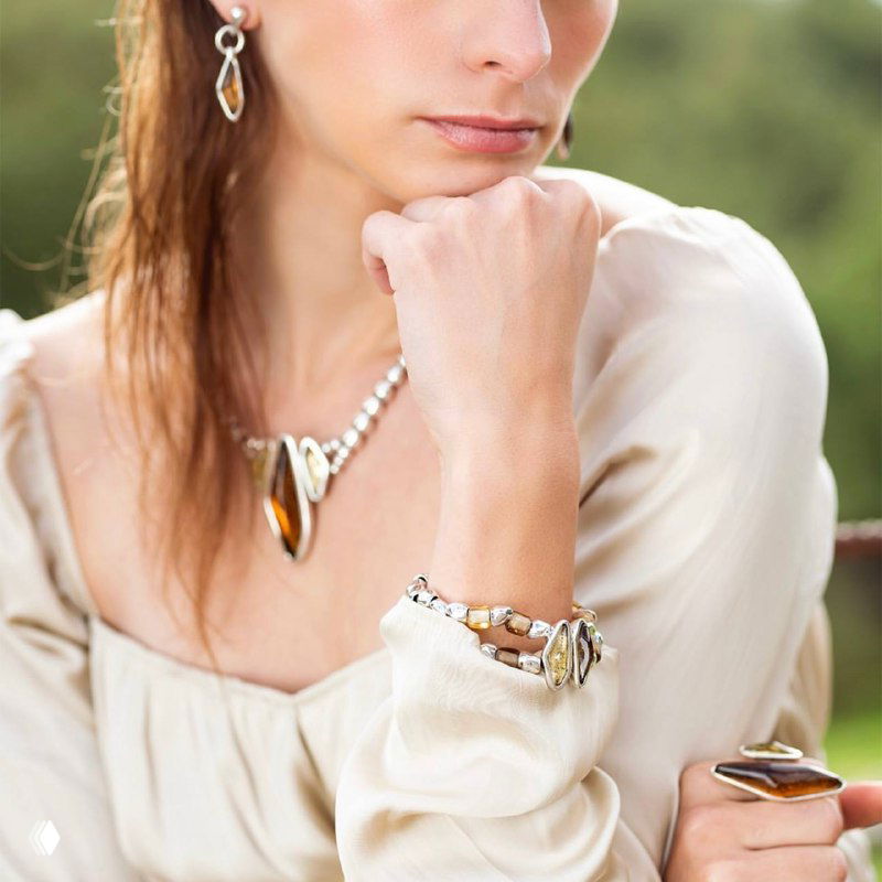 Крупный план женщины в светлой блузе с браслетом и кольцом из муранского стекла; видны детали, фактура и игра света на элементах.