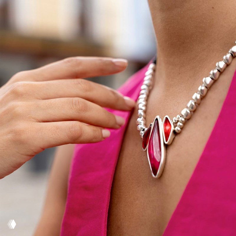 Крупный план ожерелья с крупными красными муранскими вставками на фоне розового платья; акцент на декольте и дизайне украшения.
