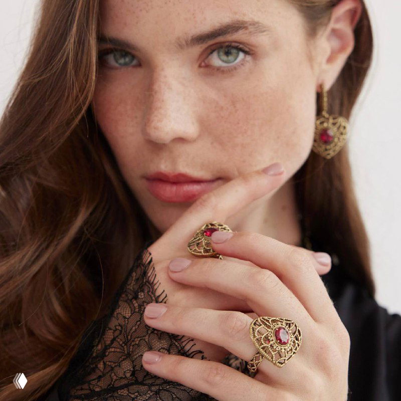 Модель в крупном плане демонстрирует кольцо и серьги AMORE ETERNO с овальным красным центром и ажурным золотистым орнаментом в винтажном стиле.