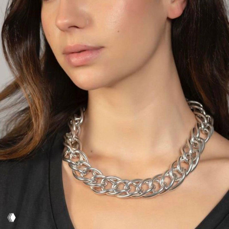 Женщина с тёмными волосами носит массивное блестящее колье-цепь крупного плетения на шее — пример, как цепь выглядит на теле