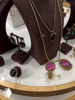 Витрина с разнообразными колье, серьгами и кольцами на бархатных стойках, экспозиция украшений разных стилей и оттенков от Claudio Canzian